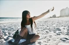 a woman sitting on the beach with her arm in the air