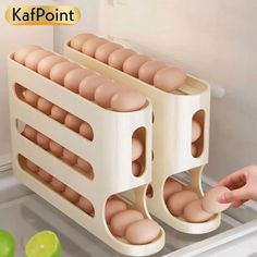 two eggs are being held in front of an open refrigerator door with the egg trays attached