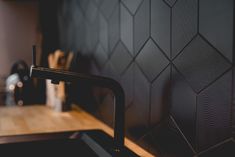 a kitchen sink with a faucet and wooden counter top in front of a black tiled wall