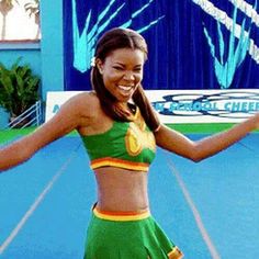 a woman in a green and yellow outfit is dancing on a tennis court with her arms outstretched