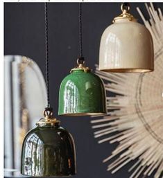 three green and white bell shaped lights hanging from a ceiling fixture in front of a mirror