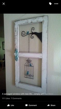 a bird in a cage is hanging on the wall next to a window with two birds inside