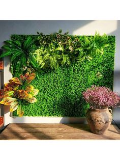 a green wall with plants and flowers on it in front of a wooden table next to a potted plant