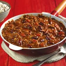 a bowl filled with chili and rice on top of a red wooden table next to a spoon