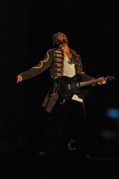 a man with a guitar in his hand and wearing a costume on stage at night