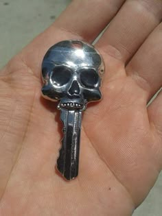 a hand holding a silver key with a skull on it