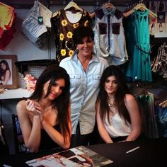 two beautiful women sitting next to each other in front of clothes on display at a clothing store