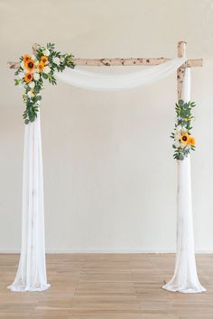 an arch decorated with sunflowers, greenery and white fabric for a wedding ceremony