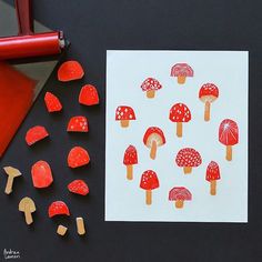 red mushrooms are arranged on white paper next to colored pencils