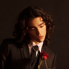 a man in a suit and tie holding a red rose with his right hand on his chest