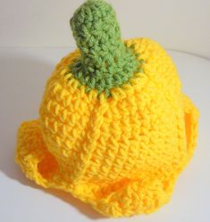 a small crocheted yellow hat with a green leaf on the top, sitting on a white surface