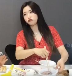 two women sitting at a table with food in front of them and one woman holding chopsticks