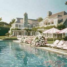 an outdoor pool with lawn chairs and umbrellas next to the swimming pool in front of a large house