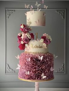 a three tiered cake with pink flowers and butterflies on top, sitting on a pedestal