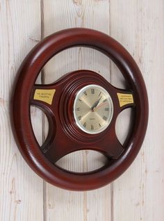 a wooden steering wheel with a clock on the front and side of it, against a white wood background