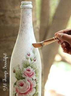 a hand holding a knife near a painted glass bottle with flowers on the outside and inside