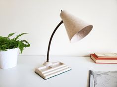 a desk lamp sitting on top of a white table next to a potted plant