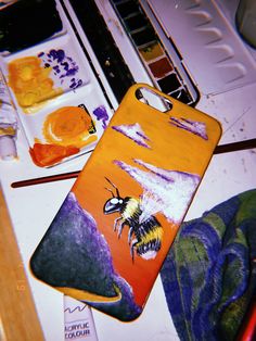 a phone case with a painting of a bee on it next to some paintbrushes