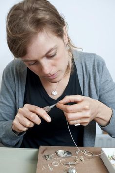 a woman sitting at a table working on some jewelry