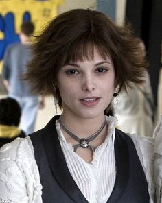 a woman with short hair wearing a white shirt and black vest is looking at the camera