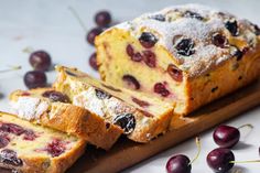 a loaf of bread with cherries and powdered sugar sits on a cutting board