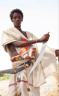 a man holding two large knives in his right hand and standing on a dirt road