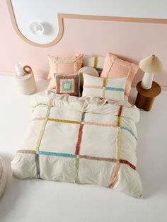 a bed with pillows and blankets on top of it in front of a pink wall