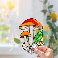 a hand holding up a stained glass piece with a mushroom and leaves design on it