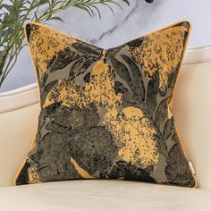 a yellow and black pillow sitting on top of a white couch next to a potted plant