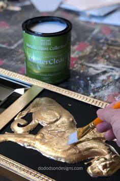 a person is painting gold foil on a black and gold tray with a paintbrush