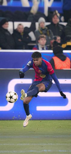 a man kicking a soccer ball on top of a field with people watching in the stands