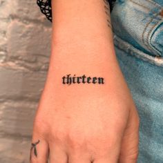 a person with a tattoo on their arm that says thirteen in cursive font