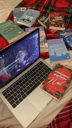 a laptop computer sitting on top of a bed covered in books and christmas themed covers