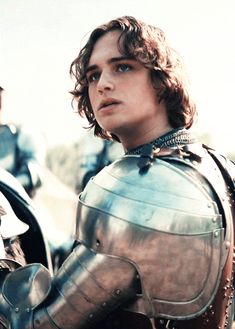 a young man dressed in armor and holding a helmet on his shoulder while standing next to other men