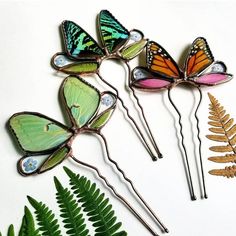 four butterfly hair pins sitting on top of green leaves