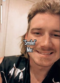 a man with long hair smiles at the camera and says smile me on his face