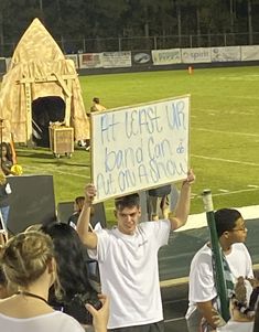 a man holding up a sign in front of a crowd at a football game on the field