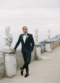 a man in a tuxedo is standing on a bridge with statues behind him