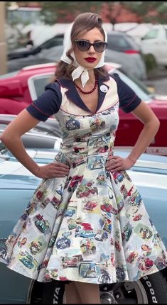 a woman standing in front of a car wearing a dress with cars all over it