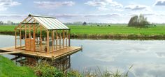 a small wooden house sitting on top of a lake next to a lush green field