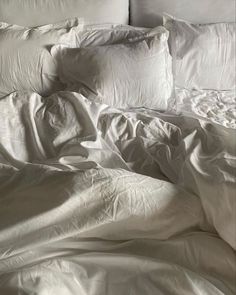 an unmade bed with white sheets and pillows