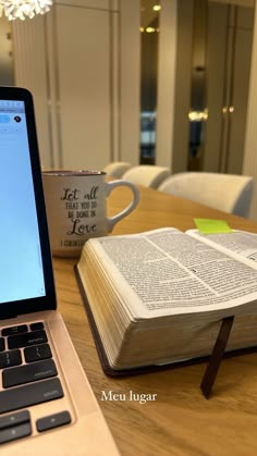 an open book sitting on top of a wooden table next to a laptop computer and coffee cup