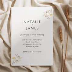 the wedding stationery is laid out on a bed sheet with dried flowers and leaves