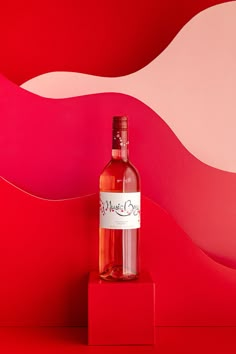 a bottle of wine sitting on top of a red block in front of a pink and white wall