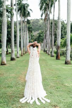 a woman in a wedding dress standing among palm trees with her hands on her head