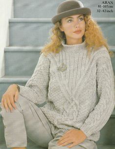 a woman sitting on the steps wearing a hat and sweater with her hands in her pockets