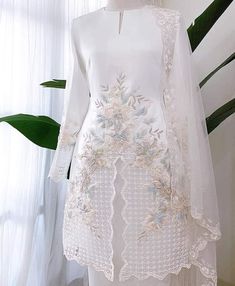 a white dress with flowers and leaves on the front, along with a veil over it