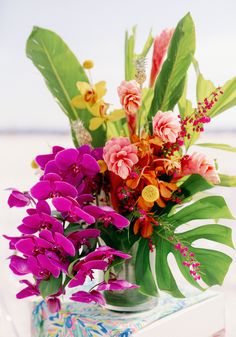 a vase filled with lots of flowers on top of a white table next to the ocean