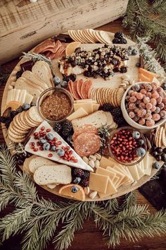 an assortment of cheeses and crackers on a platter surrounded by pine branches