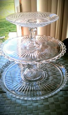 three glass cake plates sitting on top of a table next to a window with grass in the background